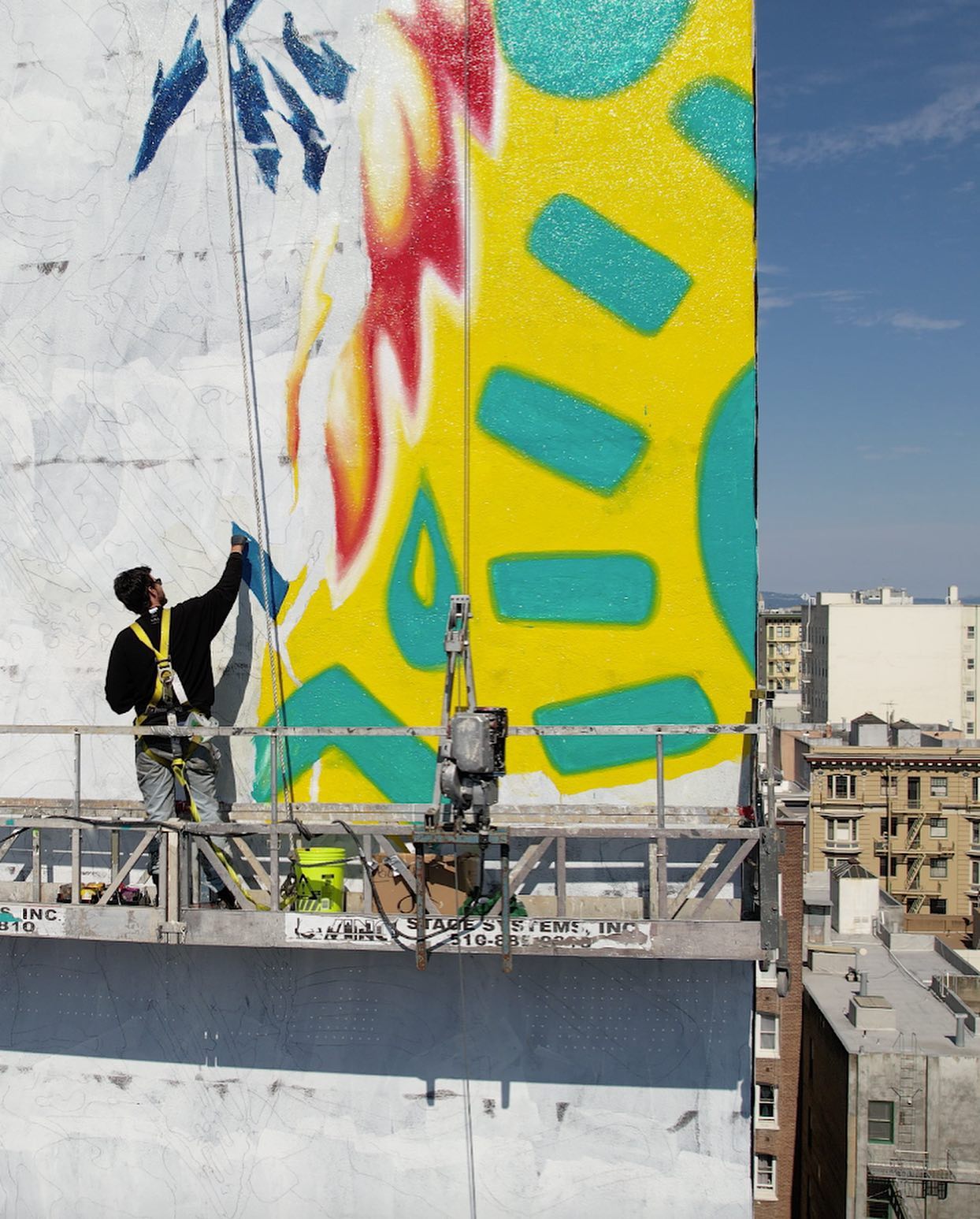 Hoist Media artist on suspended scaffold adding detail to large-scale public art mural on San Francisco building