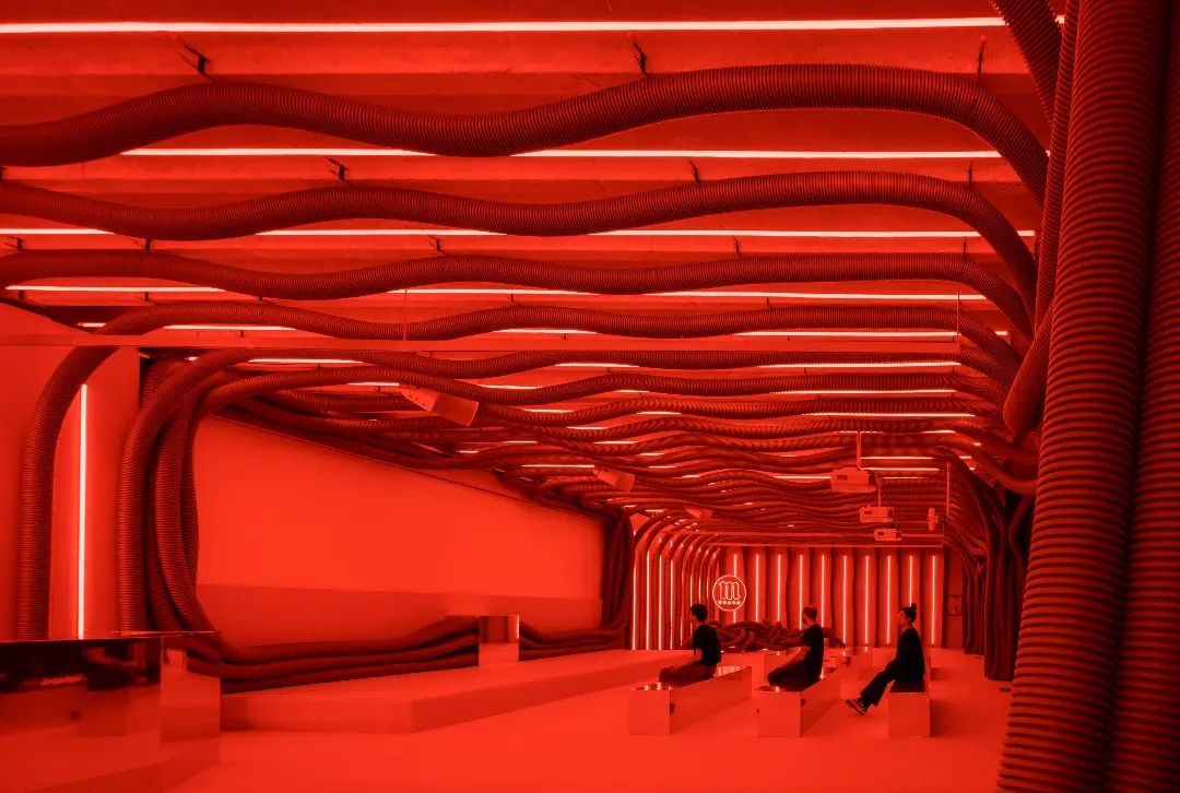 Wide view of Mahou Beer experiential activation with three people seated on benches beneath corrugated hose ceiling Madrid