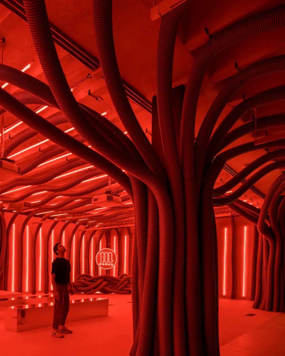 Interior view of Mahou Beer experiential activation looking down tunnel of red corrugated hoses and neon light strips with Mahou neon sign