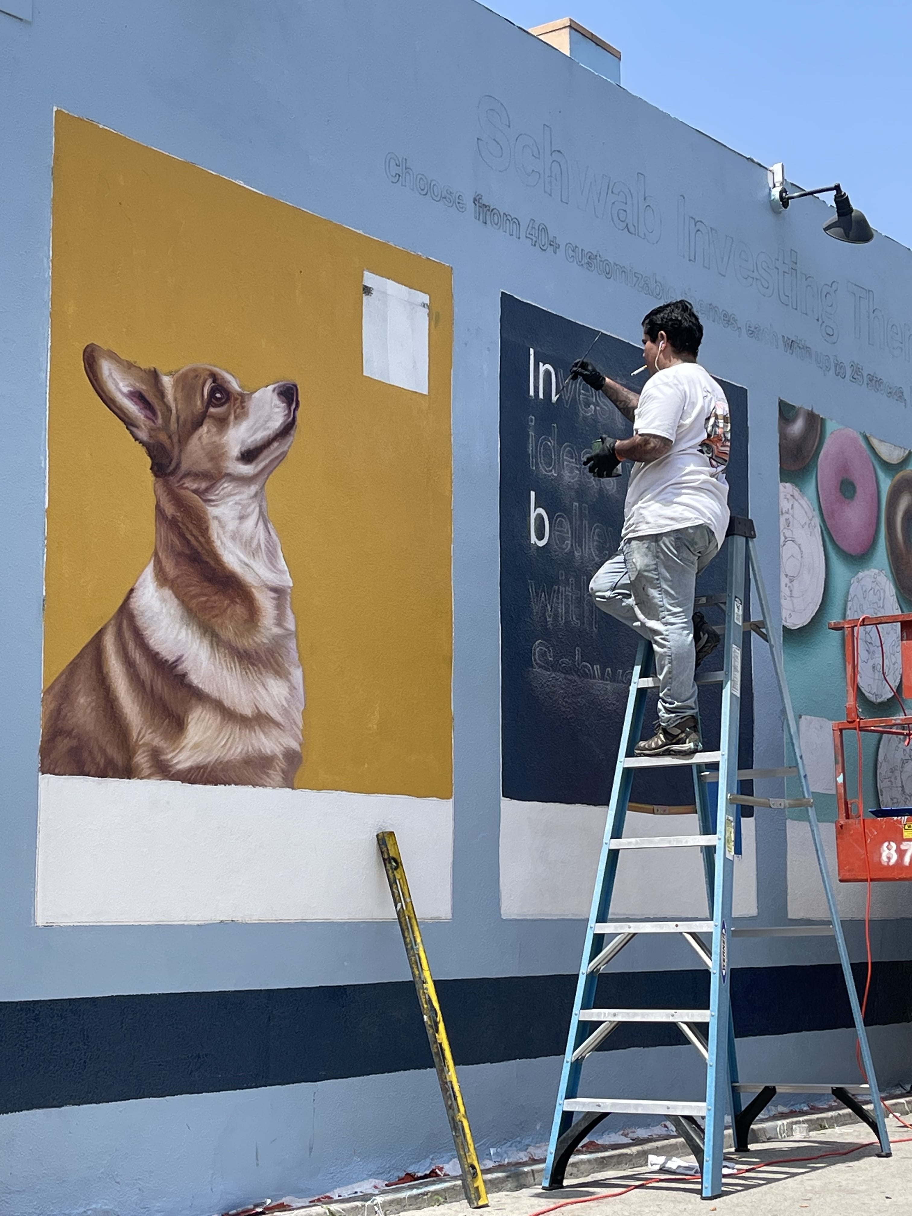 Hoist Media artist on ladder painting Charles Schwab mural text panel on building exterior in Venice California