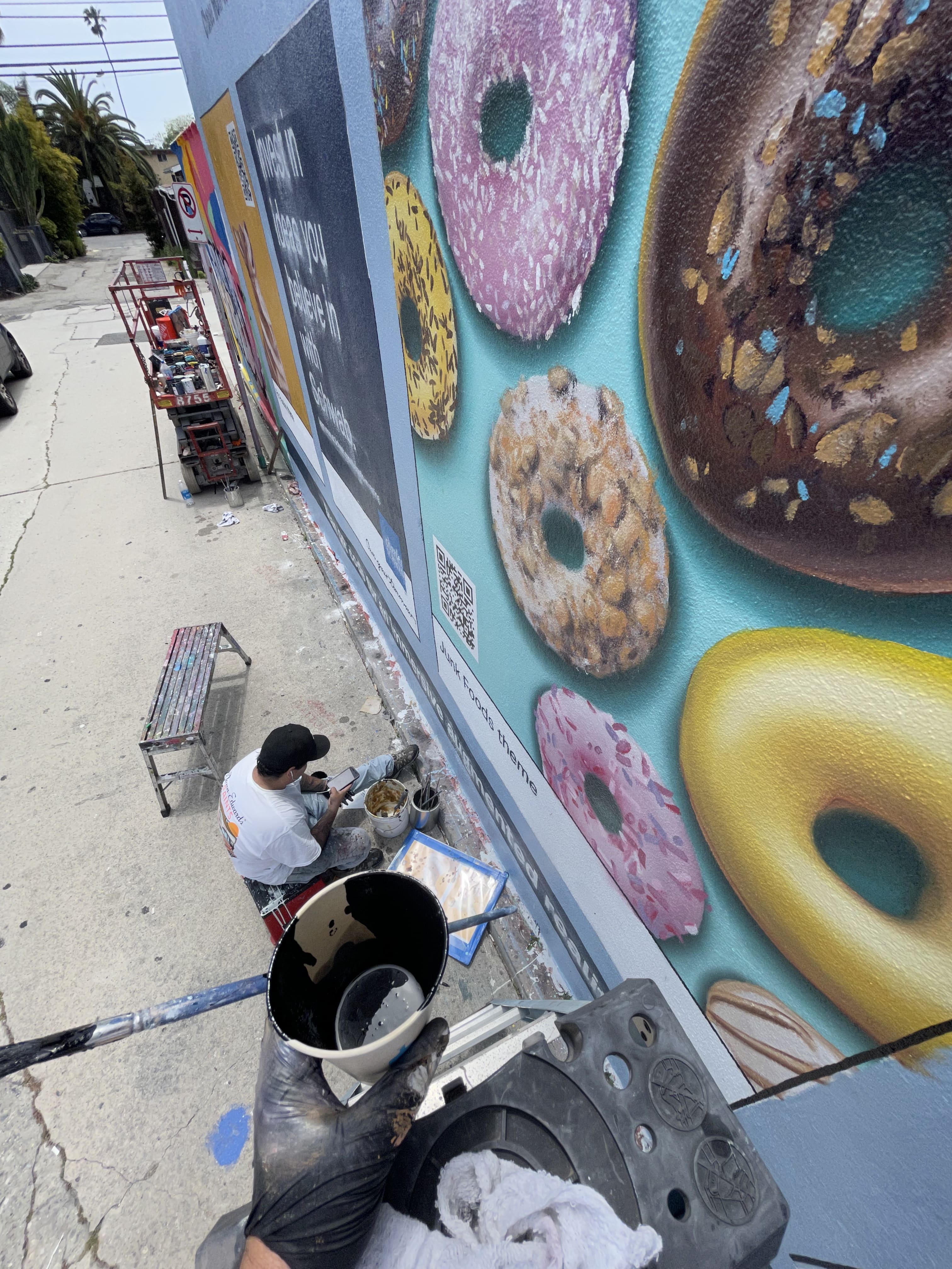 Hoist Media artist at street level painting photorealistic donut panel for Charles Schwab mural in Venice CA