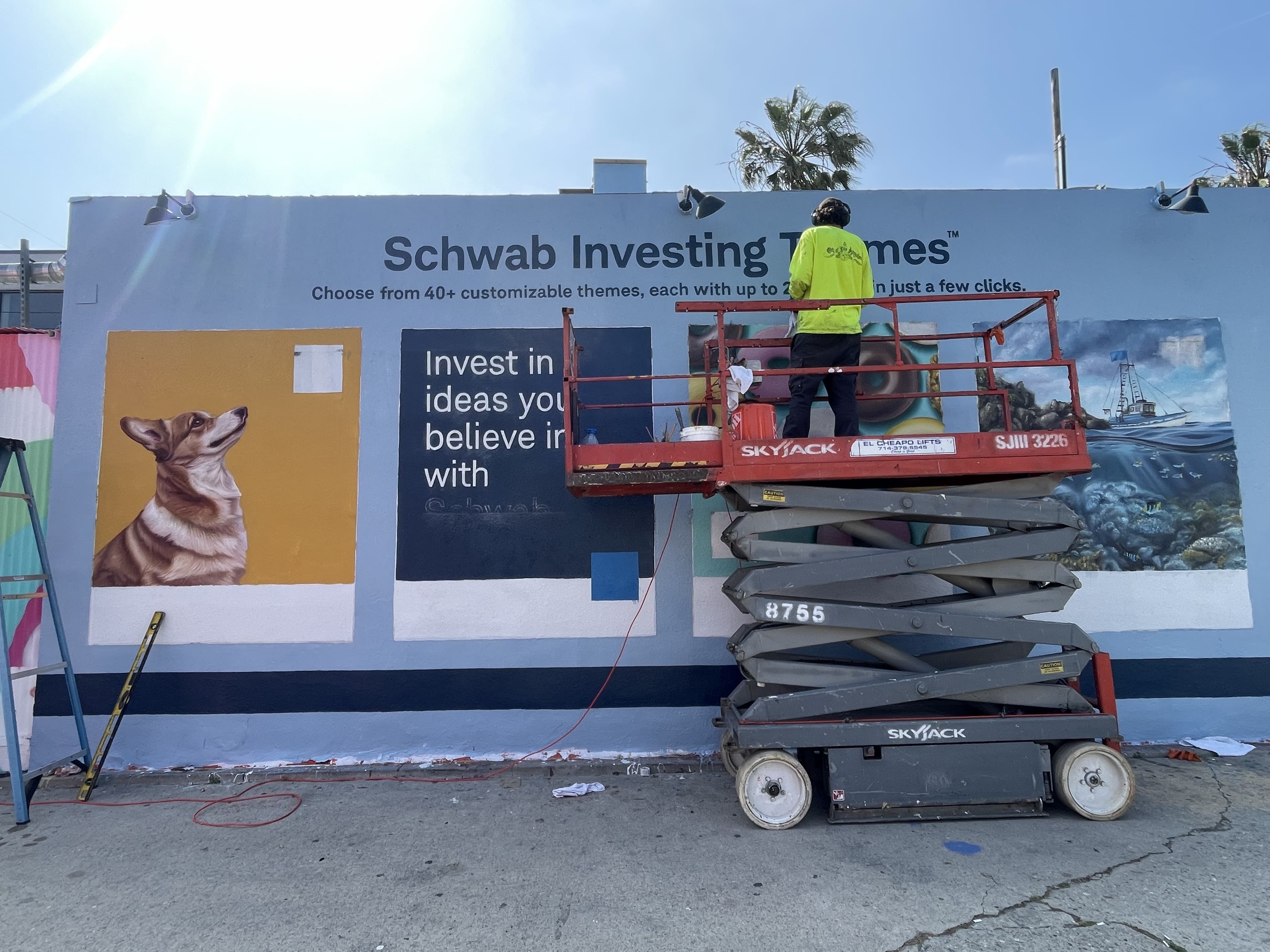Hoist Media artist on scissor lift painting Charles Schwab Investing Themes mural in progress in Venice California